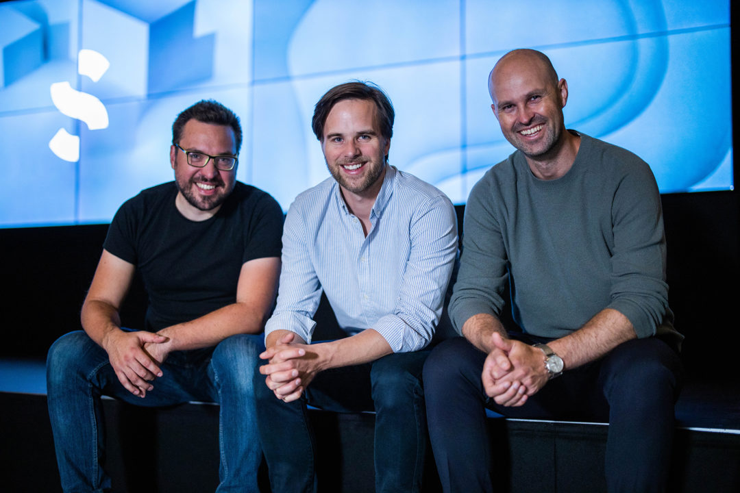 De tre skaperne av Spacemaker - Carl, Håvard og Anders - sitter tett inntil hverandre og smiler mot kamera.