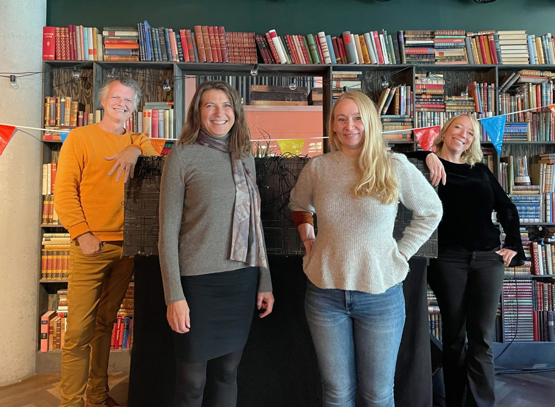 Erling Fossen, Marie Indrelid Winsvold, Marianne Netland og Maren Bjerkeng står på en scene og smiler mot kamera. De har en stor bokhylle fylt med bøker bak seg.