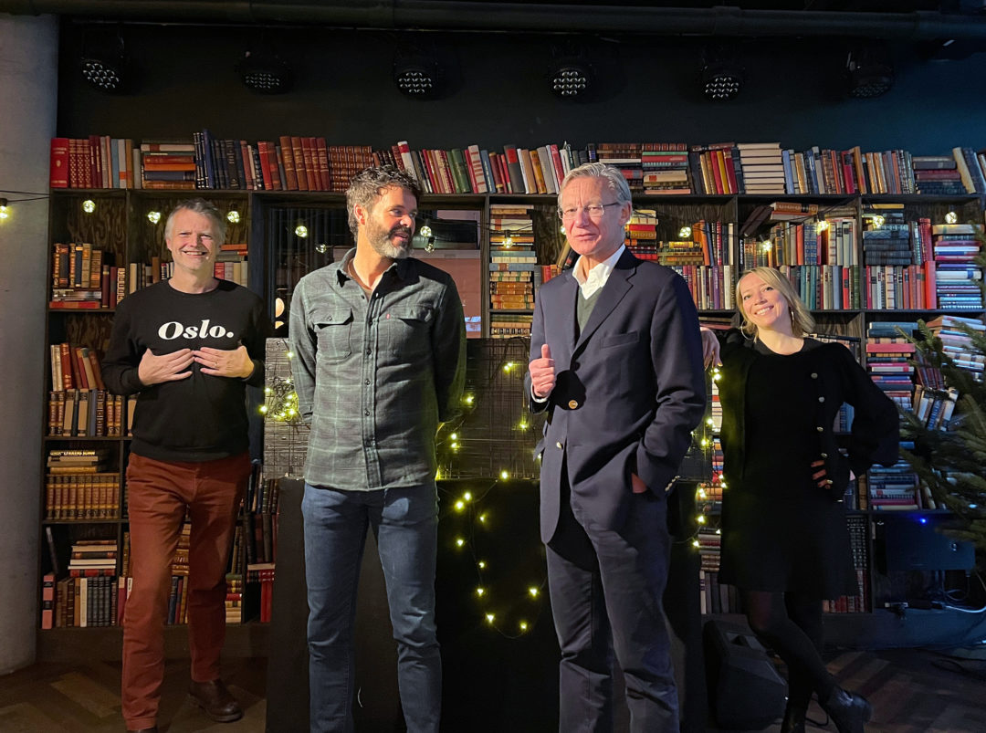 Erling Fossen, Anders Opsahl, James Lorentzen og Maren Bjerkeng står på en scene og smiler mot kamera med julelys bak seg.